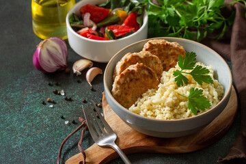 Healthy vegan food. Red fish cutlets with bulgur and fresh vegetable salad on a dark stone or slate table. Copy space.