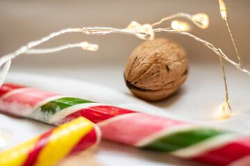 The atmosphere of Christmas and New Year. Colored candy canes, walnuts and garlands on a white background. Close-up