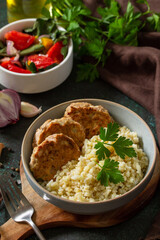 Healthy vegan food. Red fish cutlets with bulgur and fresh vegetable salad on a dark stone or slate table.
