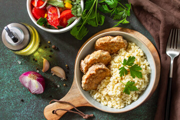 Healthy vegan food. Red fish cutlets with bulgur and fresh vegetable salad on a dark stone or slate table. Flat top view.