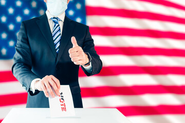Elegant man in protective mask voting for US president and thumb up with the US flag behind him