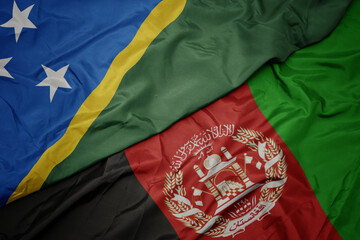 waving colorful flag of afghanistan and national flag of Solomon Islands . macro