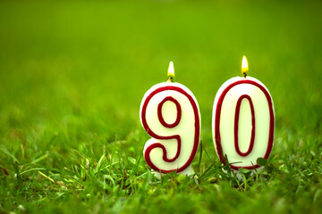 Burning candle with the number ninety on a green summer background