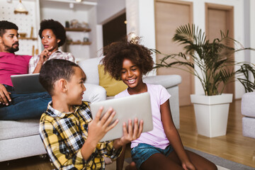 African american boy and girl lying on floor and using digital tablet. Family at home.