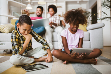 African american boy and girl lying on floor and using digital tablet. Family at home.