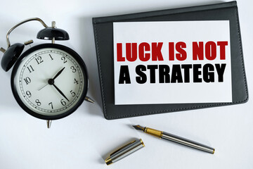 On the table there is a clock, a pen, a notebook and a card on which the text is written - LUCK IS NOT A STRATEGY