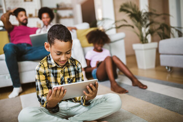 African american boy and girl lying on floor and using digital tablet. Family at home.