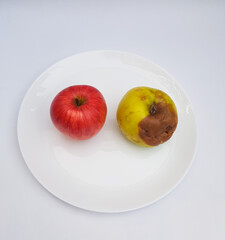Two different apples on the white plate on the wooden table, one apple is damaged