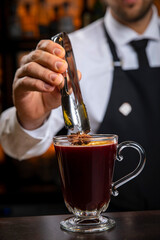 A young smiling bartender in a black apron prepares mulled wine
