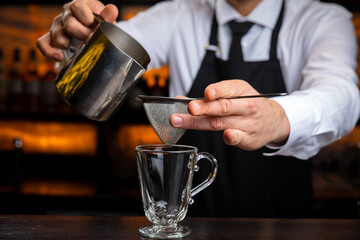 A young smiling bartender in a black apron prepares mulled wine

