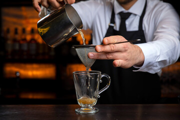 A young smiling bartender in a black apron prepares mulled wine
