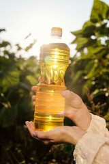 Hands of young female holding bottle of sunflower oil against green leaves