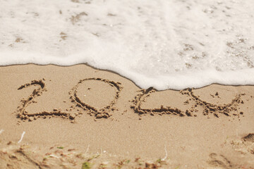 Good bye 2020 ! Wave with foam covering 2020 sign on sandy beach, leaving awful year 2020
