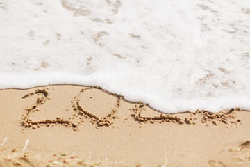 Good bye 2020 ! Wave with foam covering 2020 sign on sandy beach, leaving awful year 2020