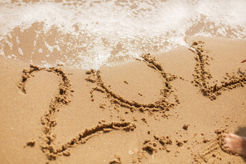 Person writing 2020 sign on sandy beach and wave foam covering and erasing 2020 inscription