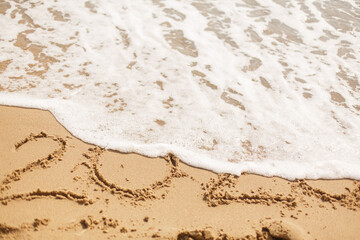 Good bye 2020 ! Wave with foam covering 2020 sign on sandy beach, leaving awful year 2020
