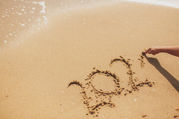 Person writing 2021 sign on sandy beach. Happy New year 2021