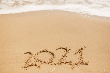 Hello 2021! Happy new year 2021 sign handwritten on sandy beach with waves and white foam