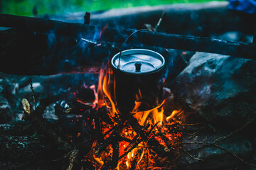 Kettle in soot hanging over fire. Cooking food at fire in wild. Beautiful firewoods burn in bonfire...