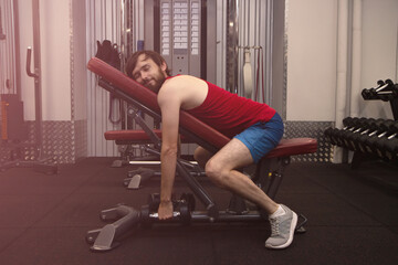 Plakat Thin sport man is tired and have break on simulator in gym