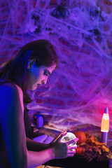 Halloween witch, young woman disguised as wicca holding a magic ball over spiderweb background with...