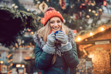 Woman in front of Christmas tree on winter market drinking hot wine - obrazy, fototapety, plakaty
