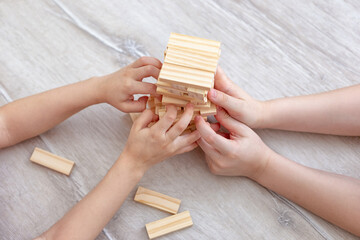 Childrens hands collects a tower of wooden blocks on the floor.