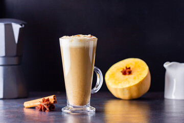 Pumpkin spice latte, coffee maker and milk jug on a dark background. Pumpkin latte with whipped cream and piece of pumpkin. Hot autumn drink