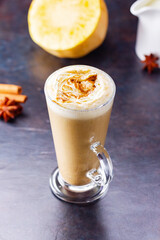 Pumpkin spice latte, coffee maker and milk jug on a dark background. Pumpkin latte with whipped cream and piece of pumpkin. Hot autumn drink