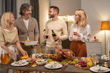 Happy young man with bottle and glass of red wine looking at his parents