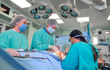 Surgeon performing cosmetic surgery on breasts in hospital operating room. Surgeon in mask wearing...