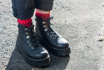 Black leather boots with red socks and black pants with a grey asphalt back ground. Alternative an indie fashion style.