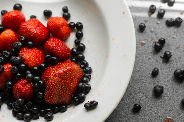 Picture of fresh berries in a white ceramic plate on grey background
