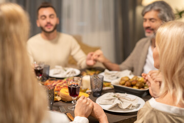 Contemporary family of four sitting by served Thanksgiving table and praying