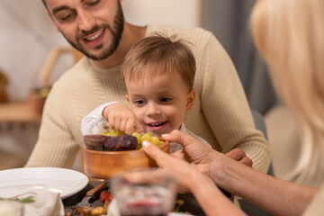 Happy young man with cute little son on his knees looking at him taking grape