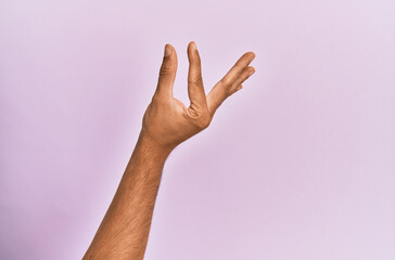 Arm and hand of caucasian young man over pink isolated background picking and taking invisible thing, holding object with fingers showing space