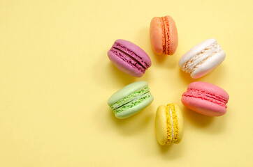 Sweet and colorful multicolored almond French macaroons on a yellow background lined in the shape of a flower, dessert with tea or coffee. place for text. view from above.