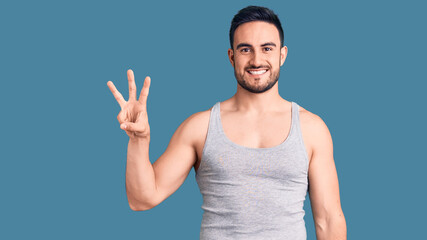 Young handsome man wearing swimwear and sleeveless t-shirt showing and pointing up with fingers number three while smiling confident and happy.