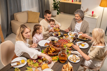 Young father giving fresh fruits to his little son by large served festive table