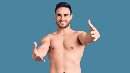 Fototapeta premium Young handsome man wearing swimwear looking at the camera smiling with open arms for hug. cheerful expression embracing happiness.