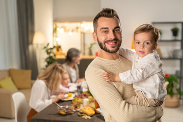 Happy young father with his cute little son on hands standing in front of camera