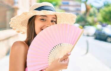 Fototapeta Young hispanic woman on vacation wearing summer style using hand fan at street of city obraz