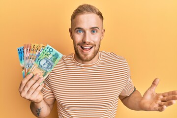 Young caucasian man holding australian dollars celebrating achievement with happy smile and winner expression with raised hand
