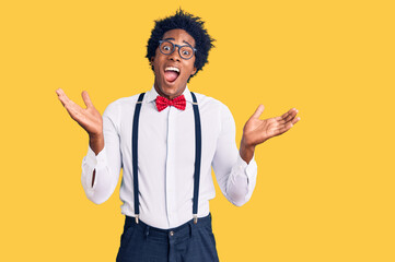 Handsome african american man with afro hair wearing hipster elegant look celebrating victory with happy smile and winner expression with raised hands