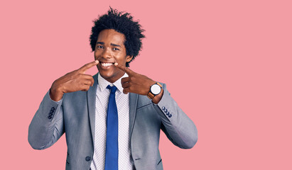Handsome african american man with afro hair wearing business jacket smiling with open mouth, fingers pointing and forcing cheerful smile