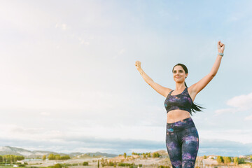 Woman standing with her hands up, reaching the top. Successful female runner with open arms on top of the mountain. Magnificent summer landscape.