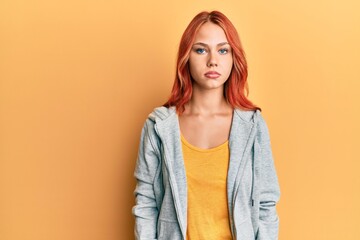 Young beautiful redhead woman wearing casual sporty sweatshirt with serious expression on face....