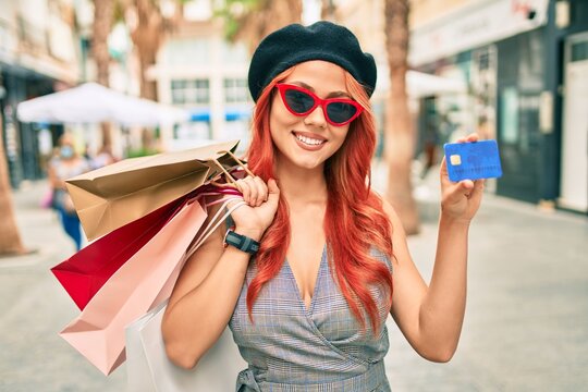 Young redhead girl wearing french style holding shopping bags  and showing credit card at the city