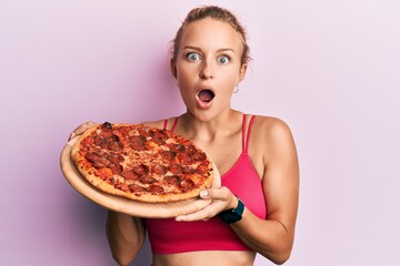 Beautiful caucasian woman holding italian pizza afraid and shocked with surprise and amazed...