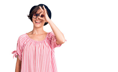 Beautiful young woman with short hair wearing casual clothes and glasses smiling happy doing ok sign with hand on eye looking through fingers